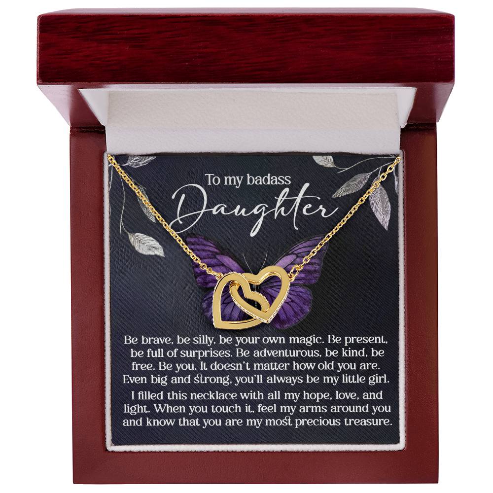 The Daughter-Big And Strong - Interlocking Hearts Necklace with a rose gold finish is beautifully presented in an open red gift box. The lid features the message: "To my badass daughter" and an inspiring note on bravery and love, enhanced by a graceful purple flower in the background.