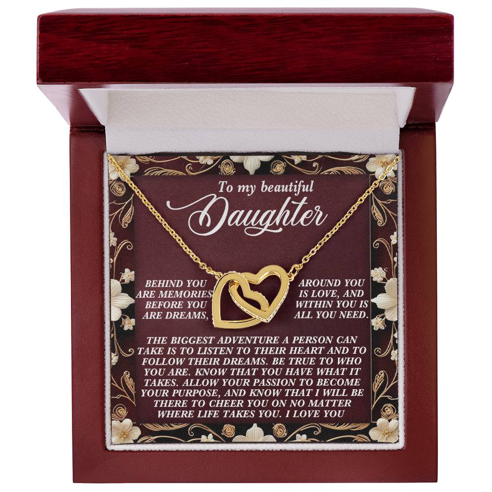 The Daughter-Follow Dreams - Interlocking Hearts Necklace features two gold hearts with cubic zirconia crystals, presented in a decorative box. The inside lid reads "To my beautiful Daughter," expressing love and support. A floral background enhances the elegant script.