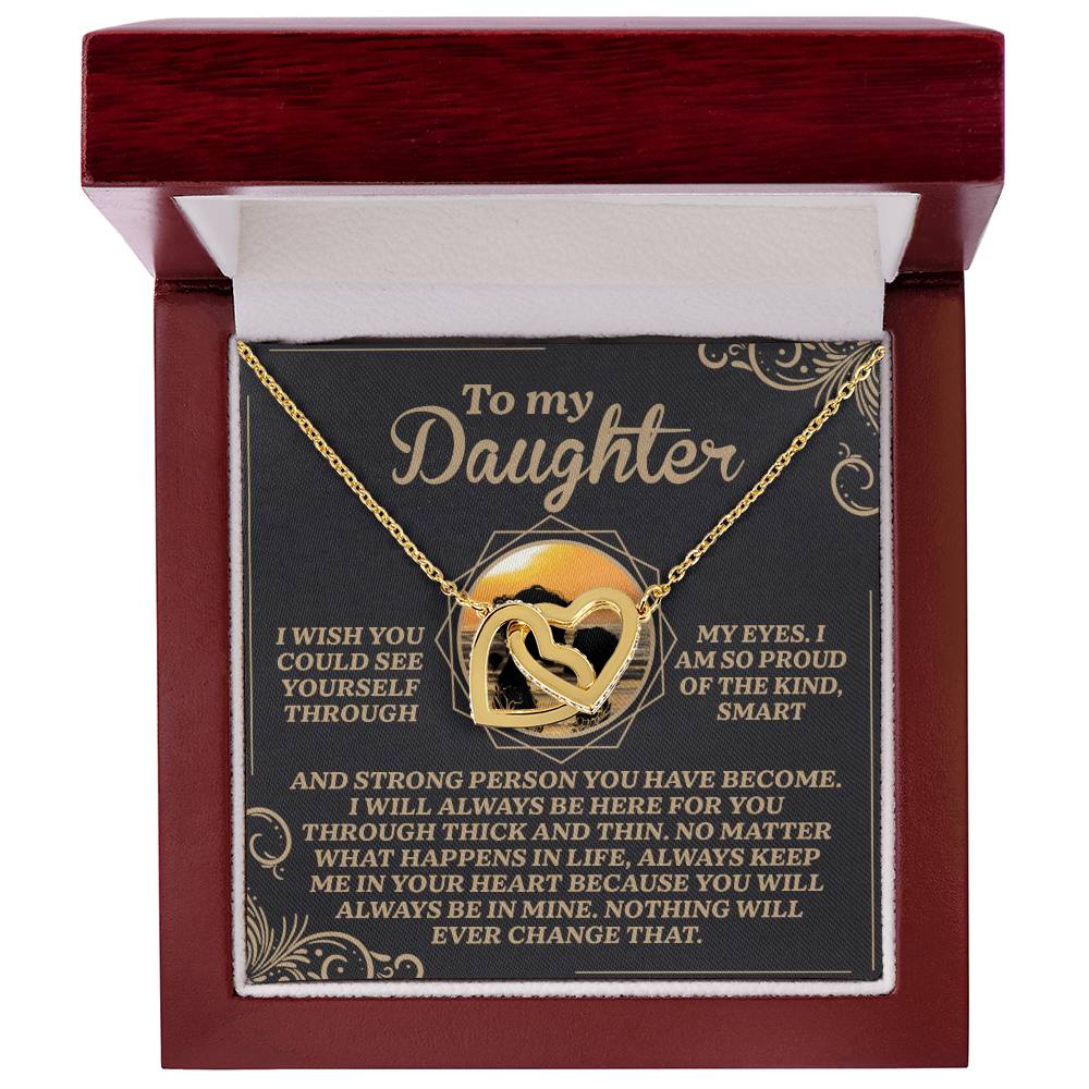 The Daughter-Proud Heart Interlocking Hearts necklace in gold, adorned with shimmering cubic zirconia crystals, is beautifully displayed in an open gift box. The lid has an inspirational message, "To my Daughter," celebrating love, pride, and unwavering support.