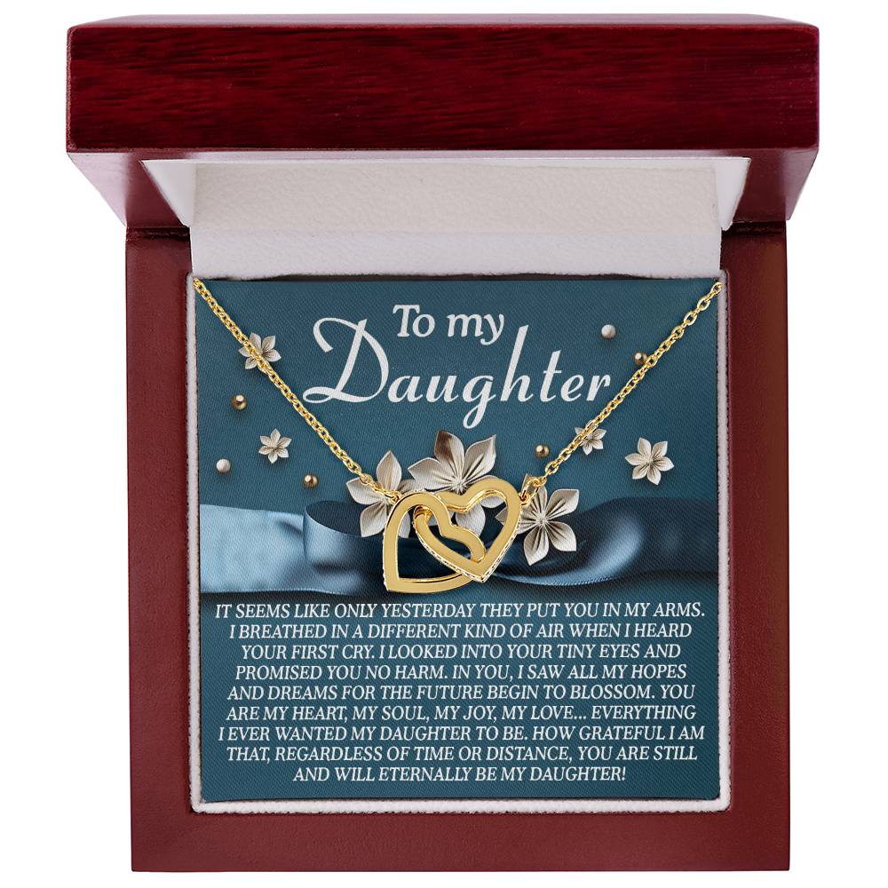 The Daughter-Hopes Dreams necklace, featuring interlocking hearts with floral accents in a rose gold finish and sparkling cubic zirconia, nestles in an open red jewelry box. The heartfelt message inside expresses love and gratitude to a daughter.