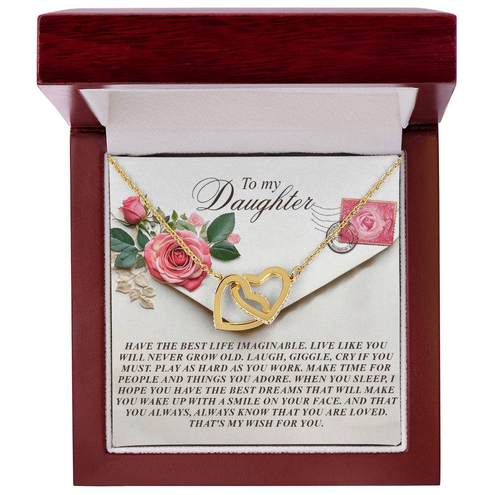 The "Daughter-My Wish - Interlocking Hearts Necklace" lies in an open box, decorated with flowers on the lid reading, "To my Daughter," and includes a heartfelt message of love, happiness, and dreams. Adorned with cubic zirconia crystals, the necklace features interlocking hearts.