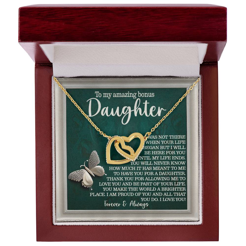 A wooden box showcases the Daughter-Your Life - Interlocking Hearts Necklace with cubic zirconia crystals. Behind it, a message for a "bonus daughter" conveys love and appreciation. The sparkling pendant and butterfly accent bring elegance to this heartfelt scene.