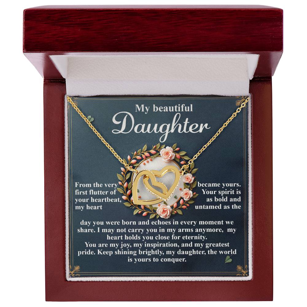 The Daughter-First Flutter - Interlocking Hearts Necklace, featuring a gold heart shape with a rose gold finish and cubic zirconia crystals, is elegantly presented in a brown box. The box reads "My beautiful daughter" alongside a sentimental message about love and inspiration, with floral accents.