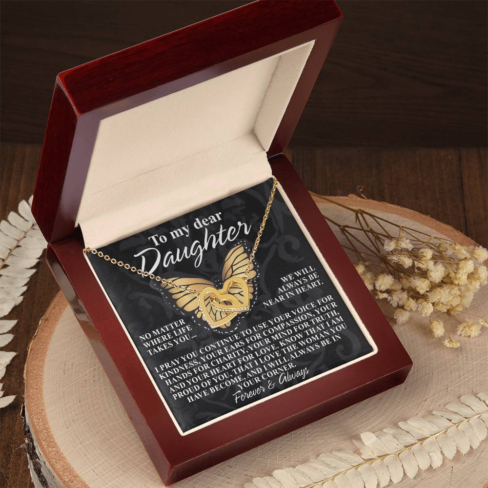 The Daughter-In Your Corner Interlocking Hearts Necklace, in rose gold with cubic zirconia crystals, lies in a red box with a heartfelt message to a daughter. The lid's surface is embellished with decorative leaves and flowers.