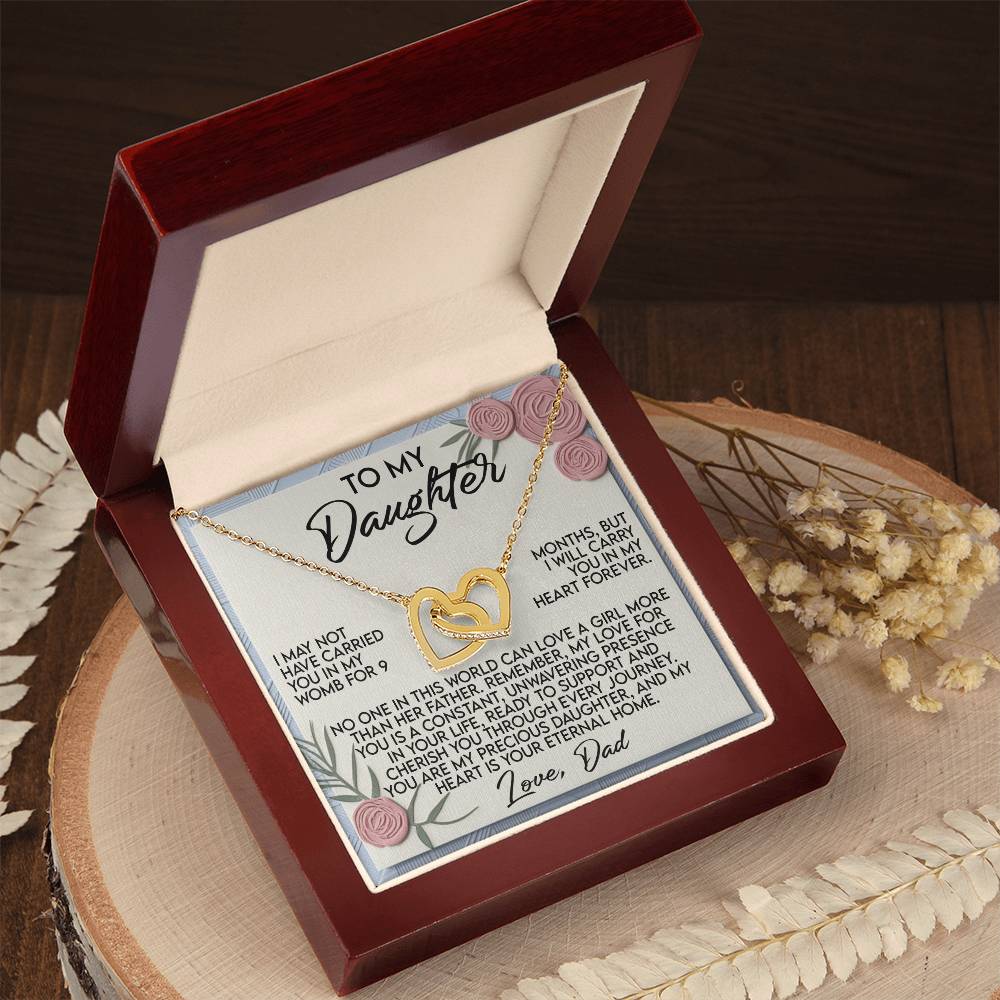 The Daughter-Eternal Home - Interlocking Hearts Necklace, adorned with cubic zirconia crystals, is revealed inside an open jewelry box. A heartfelt dad-to-daughter message is framed by pink rose accents within the lid, resting on a wooden surface surrounded by dried flowers and foliage.