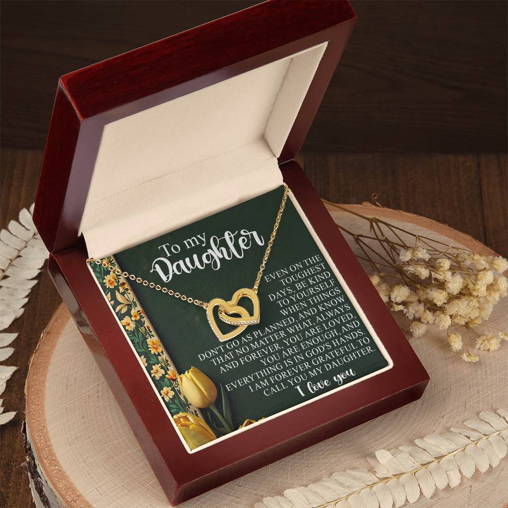 The Daughter-Tough Days - Interlocking Hearts Necklace comes in a jewelry box, accented with cubic zirconia and featuring a heartfelt "To my daughter" message on the lid. It's set on a round wooden surface with dried flowers for added nostalgia.