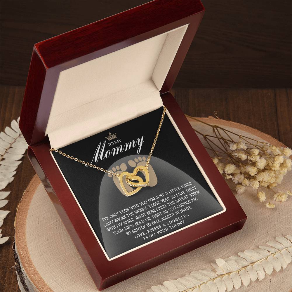 The "To Mama To Be, I Love You - Interlocking Hearts Necklace" in rose gold, featuring a heart pendant adorned with cubic zirconia crystals, is showcased in a wooden jewelry box with an engraved message to "Mommy" on the interior lid.