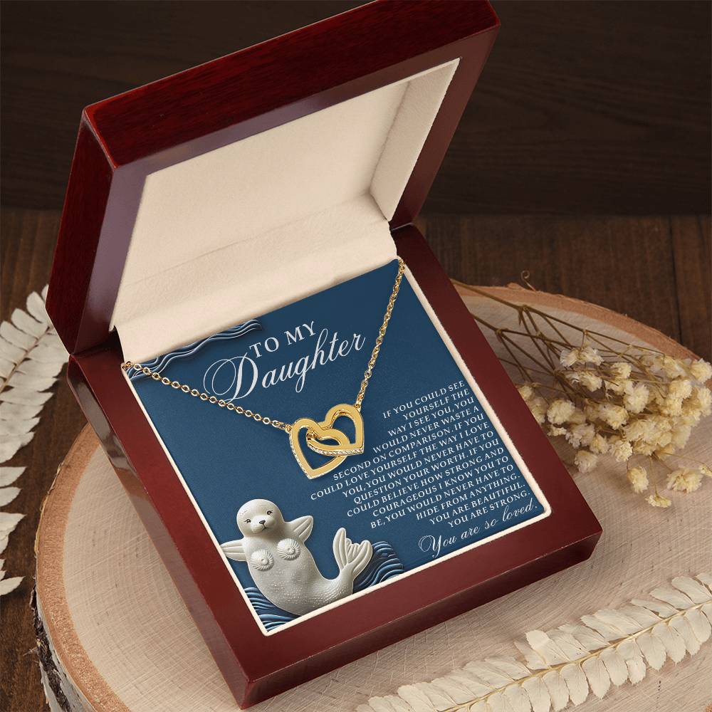 A rose gold Daughter-So Loved Interlocking Hearts Necklace sparkles in a red jewelry box. The lid shows a seal and baby illustration with "To My Daughter" message, complemented by dried flowers for a heartfelt gift.