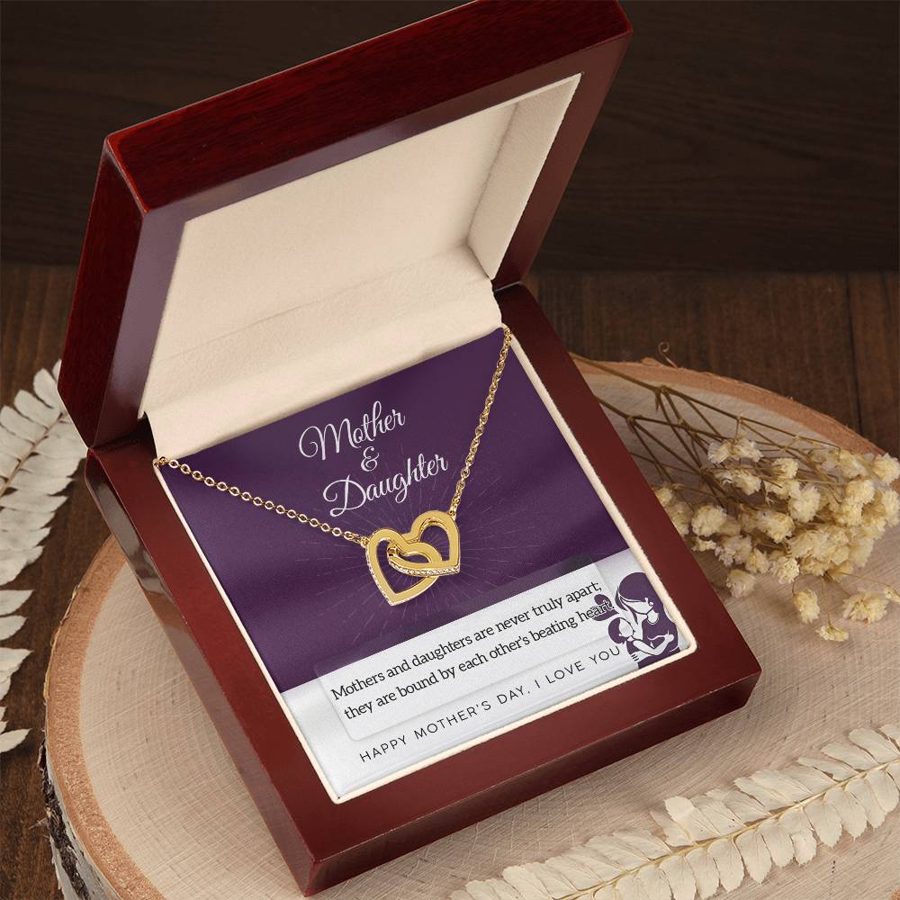 The Mother & Daughter-Never Truly Apart - Interlocking Hearts Necklace with sparkling cubic zirconia crystals is displayed in an open red box. A card reading “Mother & Daughter” celebrates their bond, with dried flowers nearby on a wooden surface.