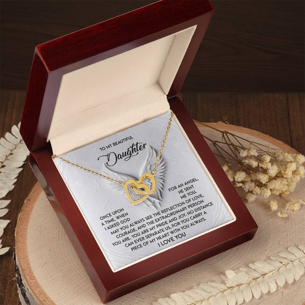 Inside a dark wooden jewelry box, the Daughter-An Angel - Interlocking Hearts Necklace with rose gold finish and cubic zirconia crystals is accompanied by a heartwarming engraved message to a daughter. Dried flowers adorn the wooden surface beside it.