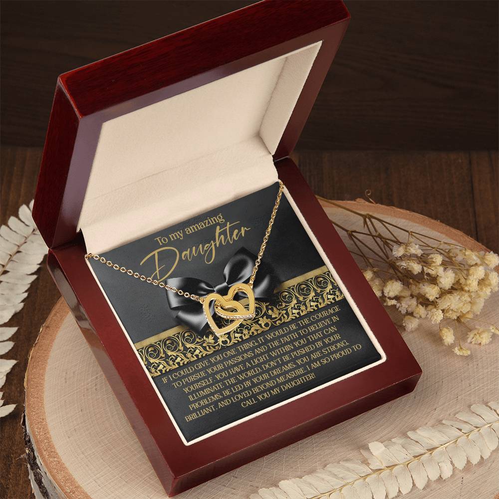 The Daughter-Pursue Passions - Interlocking Hearts Necklace, adorned with cubic zirconia crystals, is nestled in a wooden gift box. The lid has a heartfelt message to a daughter expressing love and encouragement, with dried flowers beside the box on a wooden surface.