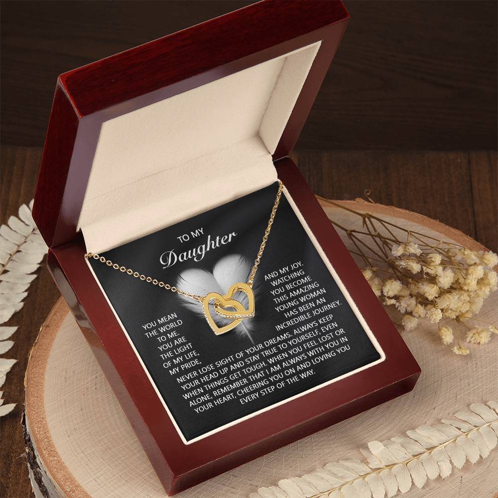 The "Daughter-In Your Heart - Interlocking Hearts Necklace" features a rose gold heart with cubic zirconia, presented open in a red box on wood. Dried flowers accompany it, and the lid bears a sentimental message for a daughter.