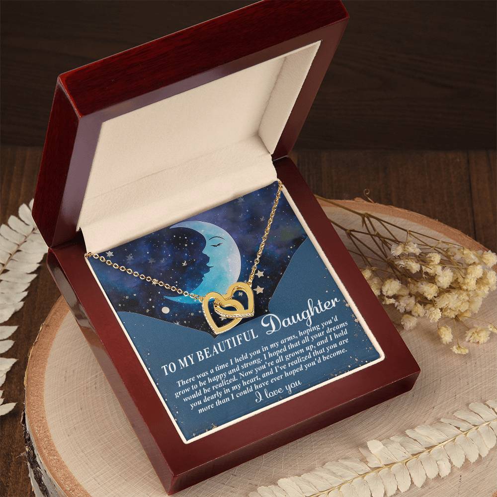 The Daughter-Grown Heart - Interlocking Hearts Necklace, featuring a surgical steel and rose gold finish, is beautifully presented in an open wooden box. The interior card, "To My Beautiful Daughter," carries a heartfelt message, while decorative dried flowers complete the display.