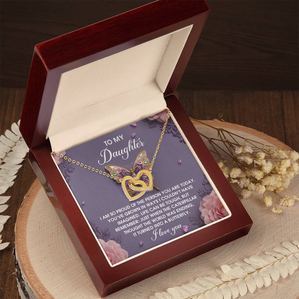 The "Daughter-A Butterfly" Interlocking Hearts Necklace in rose gold sparkles with cubic zirconia and comes nestled in an open box, featuring a heartfelt "To My Daughter" message against a floral backdrop.