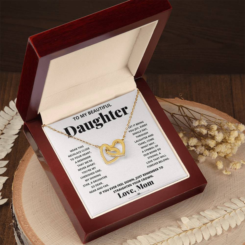 A "To My Beautiful Daughter, Wear This Necklace - Interlocking Hearts Necklace" with interlocking hearts pendants adorned with cubic zirconia crystals, presented in a box with a heartfelt message from a mother to her daughter.