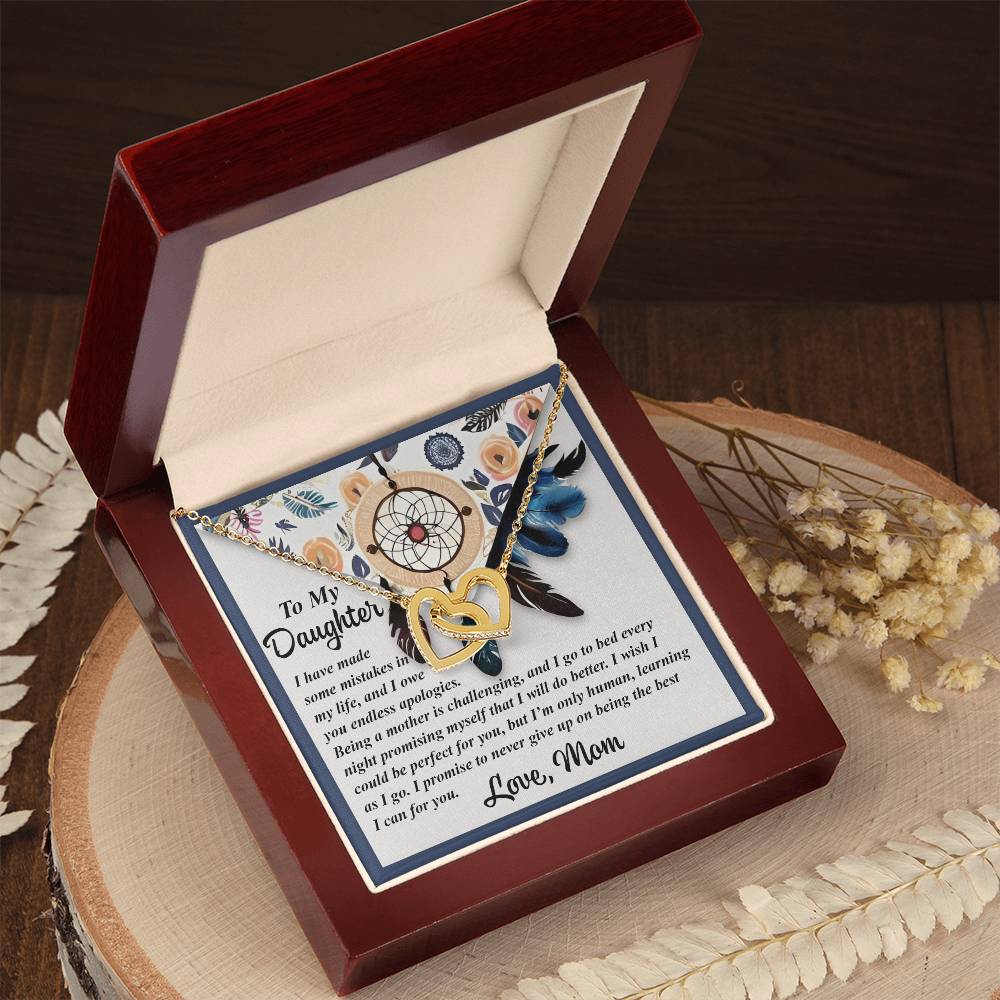Displayed in a red velvet-lined box, the "Daughter-For You - Interlocking Hearts Necklace" features a dreamcatcher pendant adorned with cubic zirconia crystals and a charming heart. It includes a heartfelt "To My Daughter" letter and is elegantly set on wood surrounded by dried flowers.