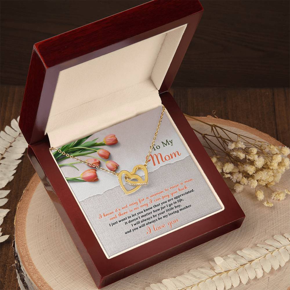The Mom-Go In Life - Interlocking Hearts Necklace, adorned with cubic zirconia crystals, is showcased in an open red velvet box featuring tulip illustrations and a "To My Mom" message on the inside lid. Dried flowers are artfully arranged nearby on a wooden surface for added sentimentality.