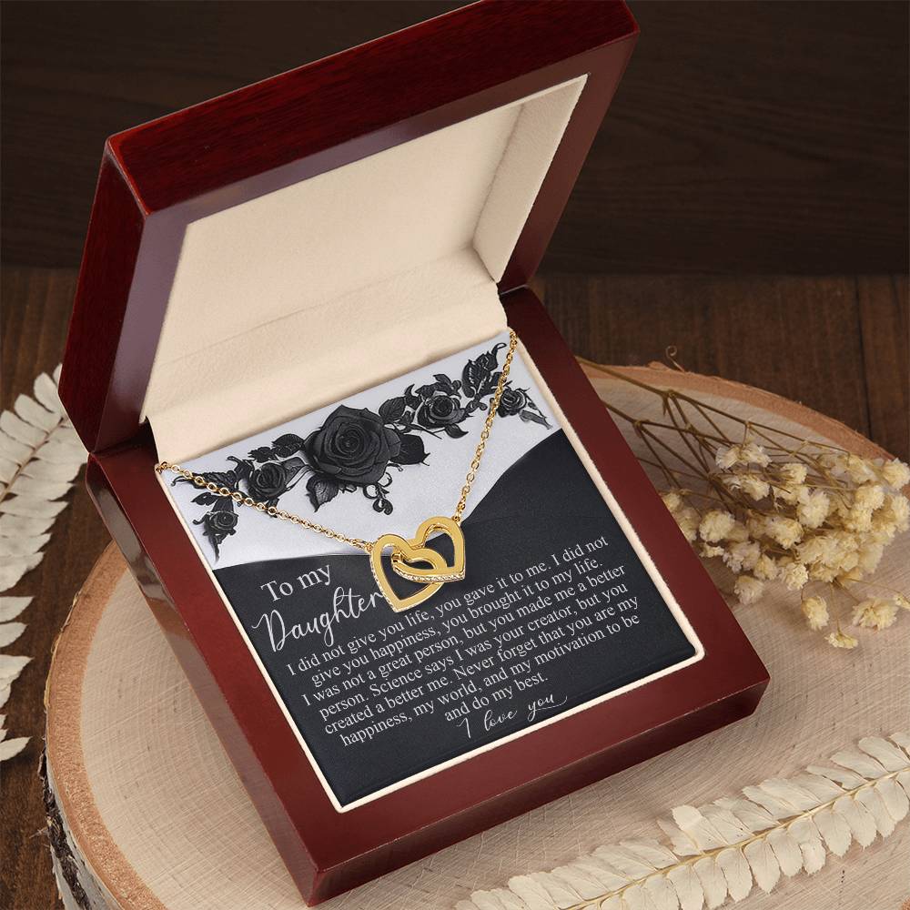 The Daughter-Better Person - Interlocking Hearts Necklace, with a gold heart shape and rose gold finish, rests in an open wooden box adorned with dried flowers. Inside, a card titled "To my Daughter" delivers an emotional message of love and support, elegantly displayed on a wooden surface.