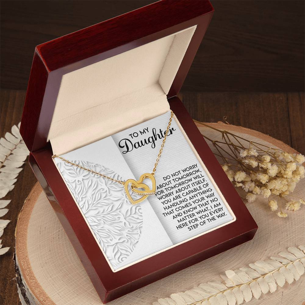 The Daughter-Tomorrow Worry - Interlocking Hearts Necklace in a gold heart shape with a rose gold finish is showcased in an open red velvet box. The heartfelt message reads: "To My Daughter...Do not worry about tomorrow...I'm here with you every step of the way," adorned with nearby fern leaves and dried flowers.