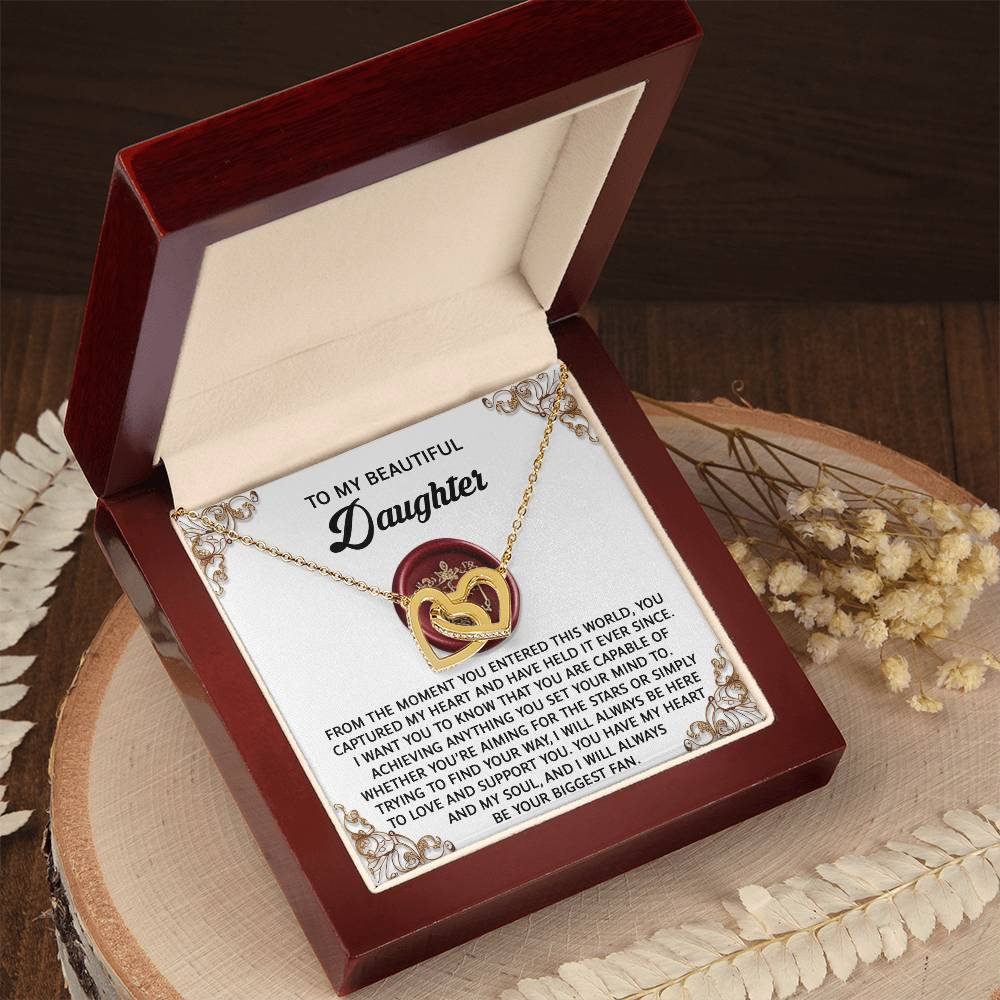 The "Daughter-Biggest Fan - Interlocking Hearts Necklace" features cubic zirconia crystals in interlocked hearts, presented in an open wooden box with a heartfelt message for a daughter.