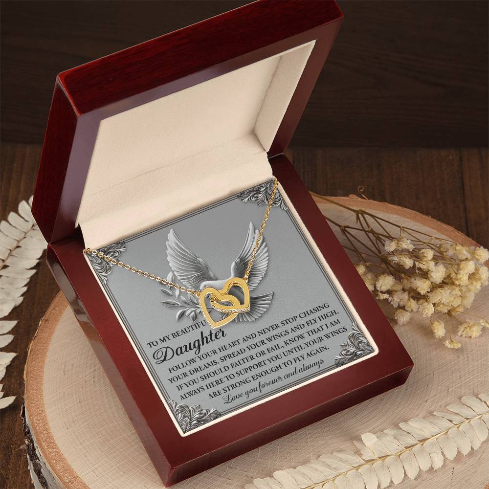 The "Daughter-Your Wings" Interlocking Hearts Necklace, adorned with stunning cubic zirconia crystals, sits in an open wooden box. A plaque reading "To My Beautiful Daughter," featuring a dove illustration, stands behind it. Dried flowers on a wooden surface enhance the display's charm.