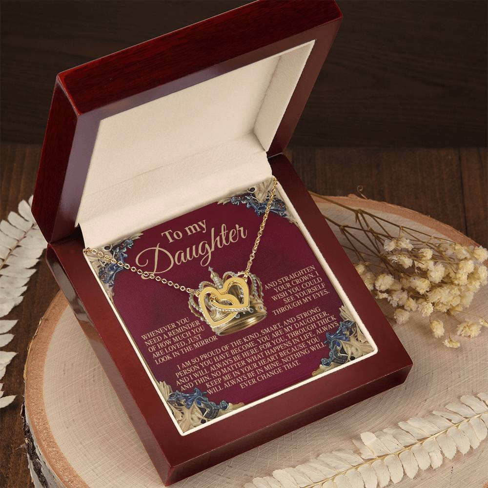 The Daughter-Straighten Crown Interlocking Hearts Necklace, with a rose gold finish, is showcased in an open, red velvet-lined wooden box. Inside the lid is a sentimental message titled "To my Daughter," and dry flowers decorate the wooden surface beside it.