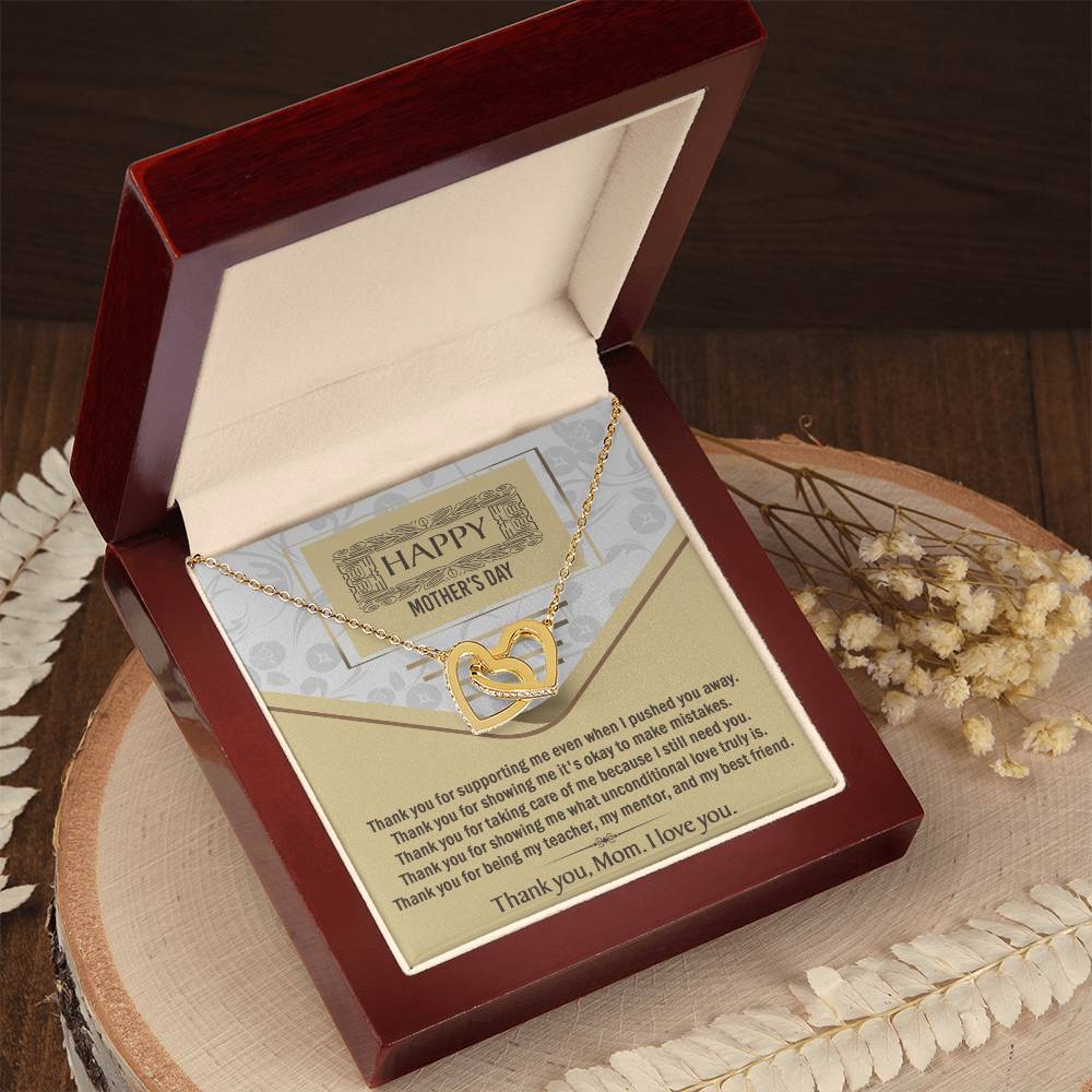 The Mother's Day-Thank You - Interlocking Hearts Necklace with sparkling cubic zirconia is displayed in a red box beside a thank you card for Mom, with dried flowers and white fern leaves on a wooden surface.