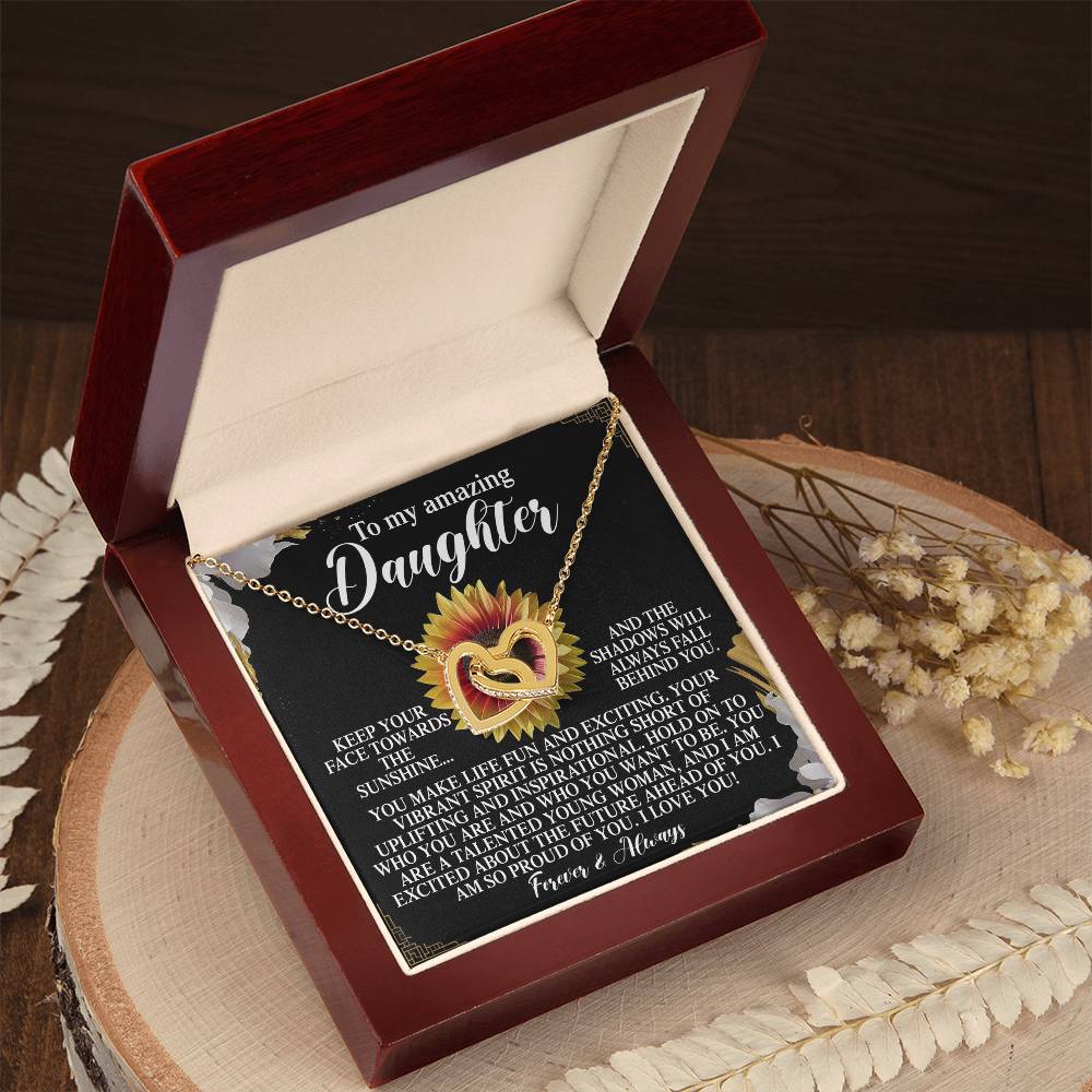 The open jewelry box reveals the "Daughter-Vibrant Spirit - Interlocking Hearts Necklace" in rose gold with cubic zirconia crystals, resting on wood alongside a sunflower, dried flowers, and a heartfelt card for a daughter.
