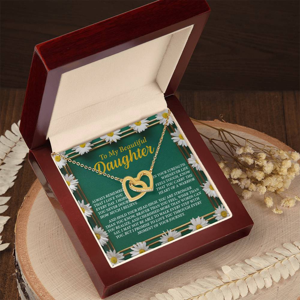 The "Daughter-Your Journey - Interlocking Hearts Necklace" in a red jewelry box features a note saying: "To My Beautiful Daughter." Made of surgical steel and rose gold, it shines with cubic zirconia crystals, displayed open on a wooden surface surrounded by dried flowers.