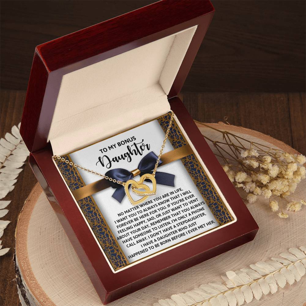 The Daughter-Have Someone Interlocking Hearts Necklace features a rose gold finish and cubic zirconia crystals. It comes in a wooden box with a heartfelt message card for your "bonus daughter" and includes elegantly placed dried flowers.