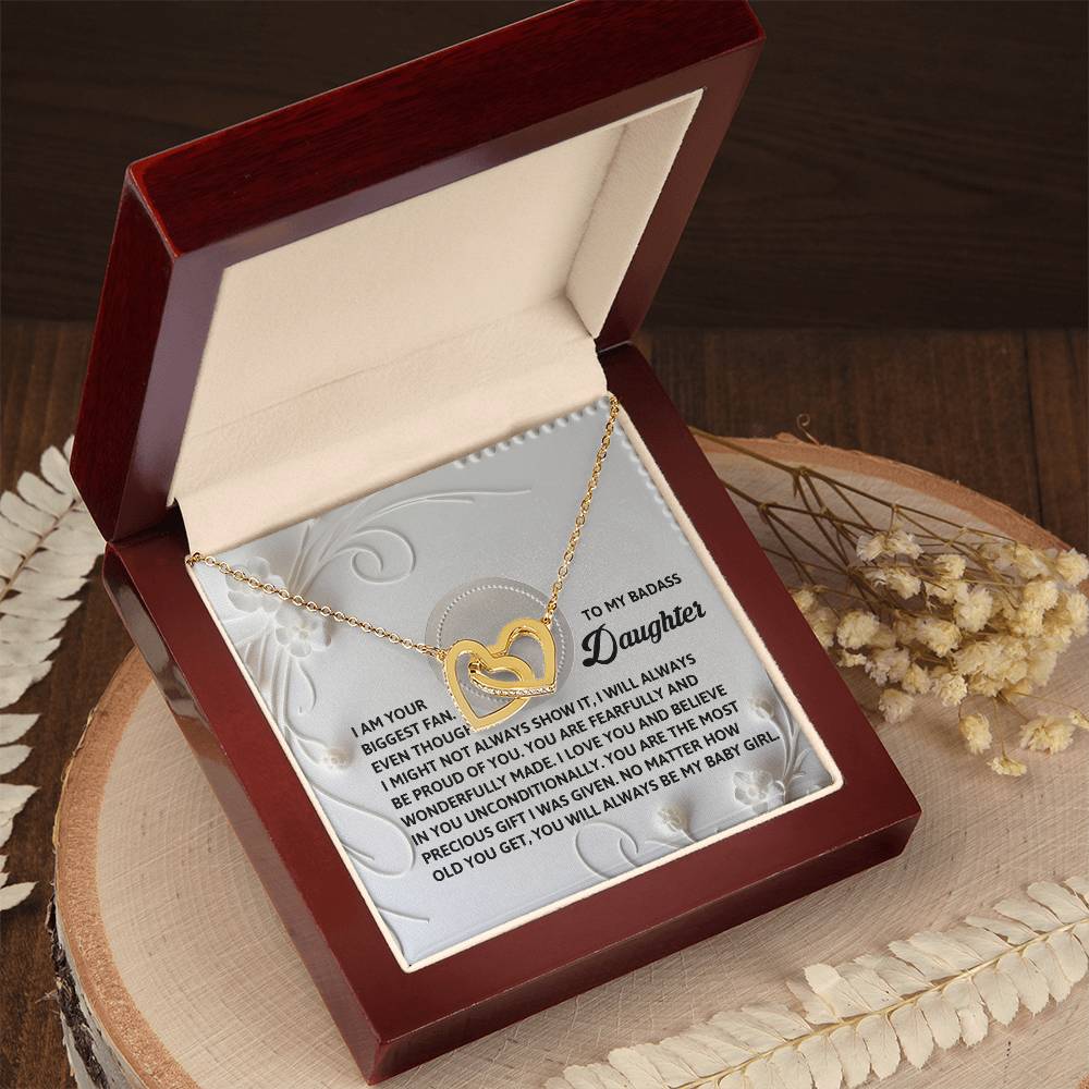 The Daughter-My Baby Girl Interlocking Hearts Necklace, featuring cubic zirconia crystals, comes in a brown display box with an engraved heartfelt message inside the lid and dried flowers, making it a perfect gift for her.