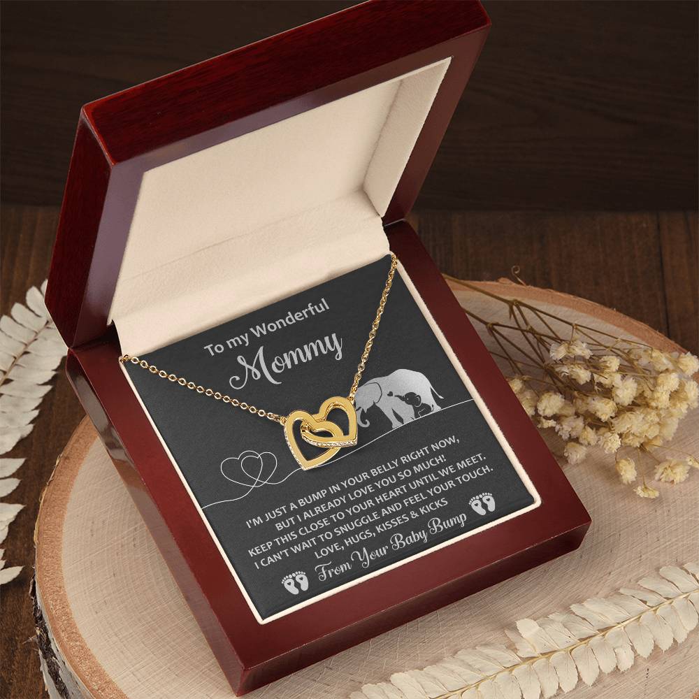 The "To Mama To Be, Until We Meet - Interlocking Hearts Necklace" features dual pendants adorned with cubic zirconia crystals, presented in a gift box with a heartfelt message 'from your baby bump.' Dried flowers elegantly accompany the box, making it a unique gift.
