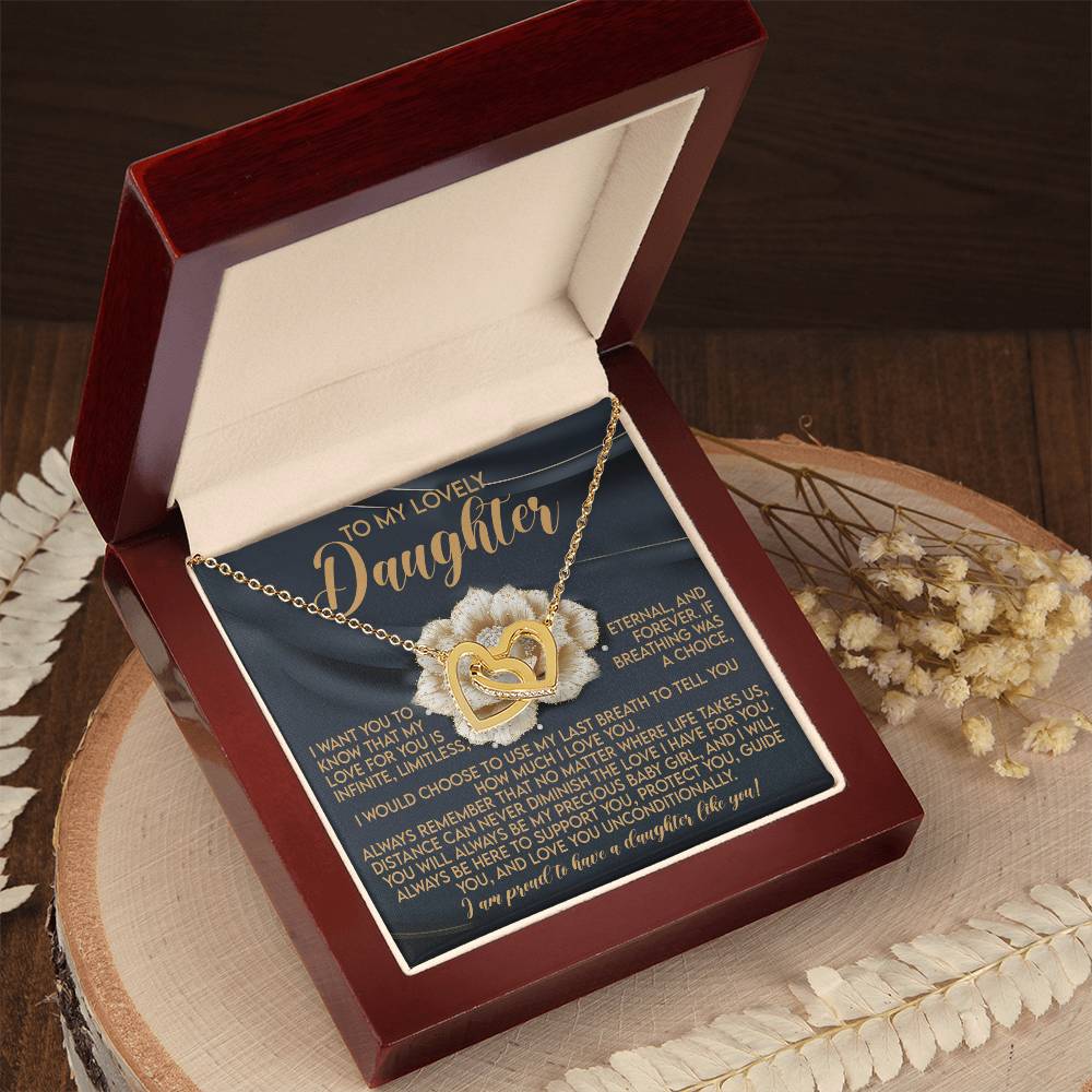 The Daughter-Infinite Love Interlocking Hearts Necklace, featuring a rose gold finish, is elegantly displayed in a wooden box with a heartfelt message card for your daughter. The open box sits gracefully on a wooden surface, surrounded by dried flowers and foliage.