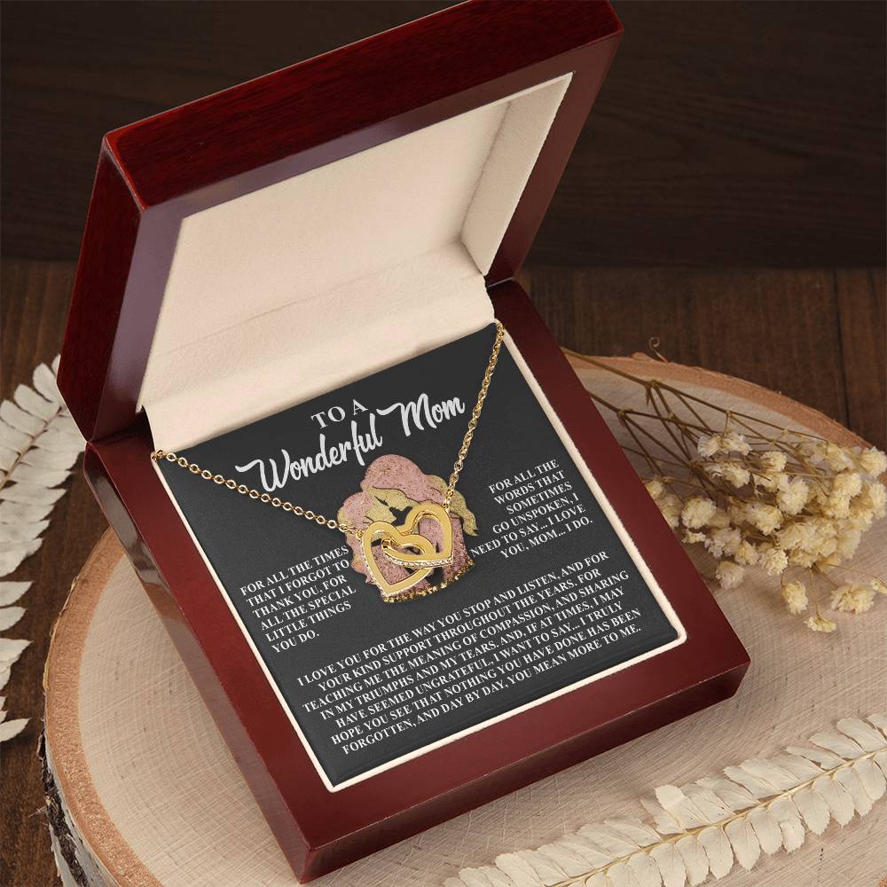 The Mom-More To Me - Interlocking Hearts Necklace, adorned with cubic zirconia crystals, rests in a red velvet box featuring a poem titled "To a Wonderful Mom." Set on wood and framed by dried flowers, it's the perfect gift for her.