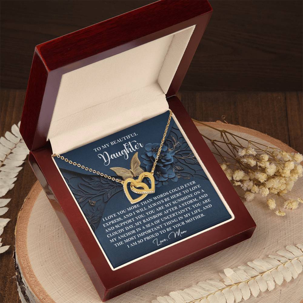 The "Daughter-In My Life - Interlocking Hearts Necklace" features a rose gold finish and comes nestled in a wooden box, paired with an ornate card for a daughter and surrounded by decorative dried flowers.
