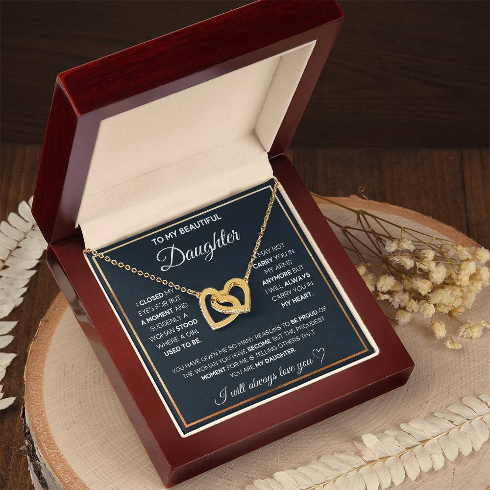 A "To My Daughter, I Will Always Carry You In My Heart - Interlocking Hearts Necklace" by ShineOn Fulfillment, presented in a red box on a wooden surface, featuring interlocking hearts and cubic zirconia crystals.