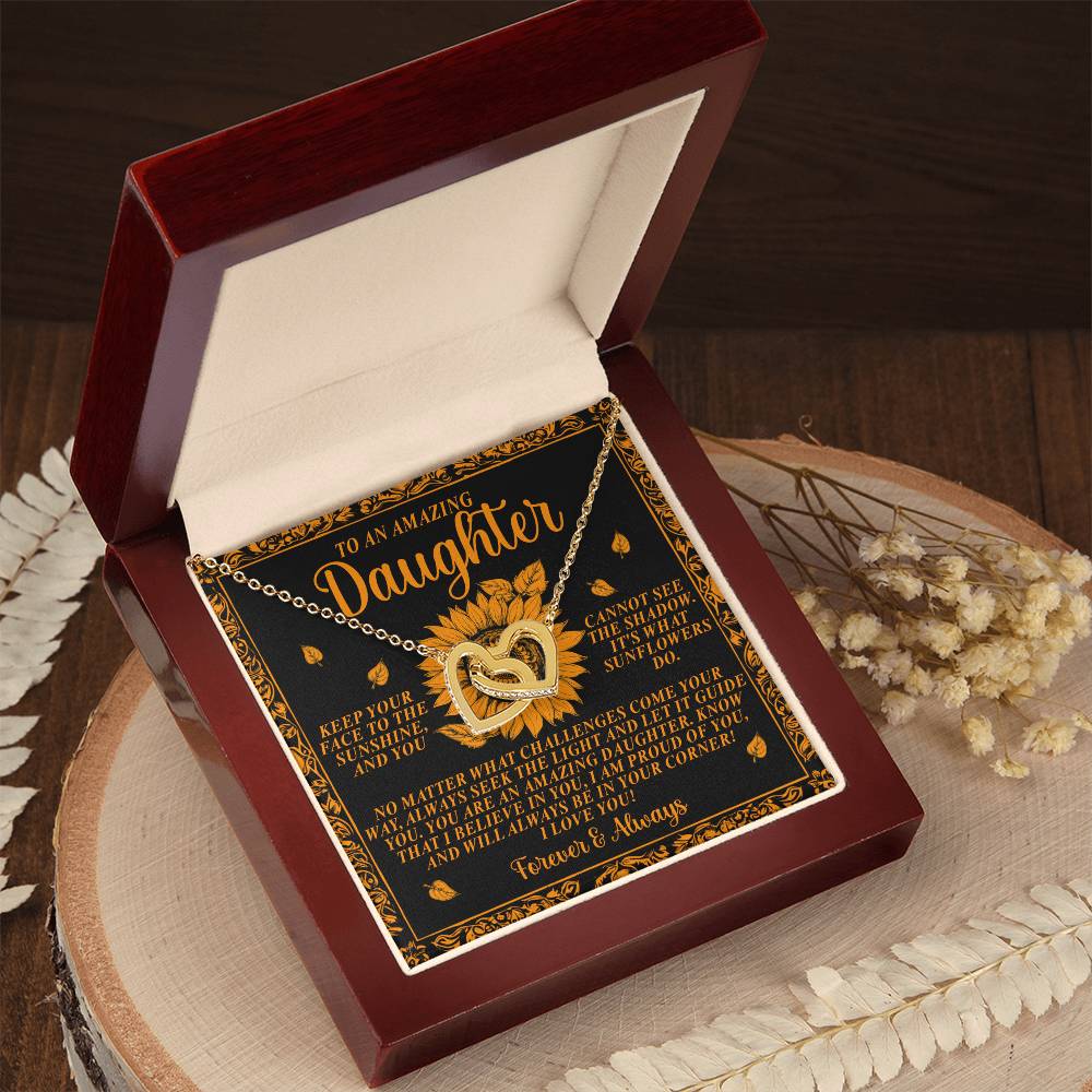 The "Daughter-Seek Light" Interlocking Hearts Necklace, featuring rose gold finish with sunflower pendants, is nestled in a wooden box. A heartfelt message of love and encouragement for a daughter is inside the lid. Delicate dried flowers beside the box add extra charm.