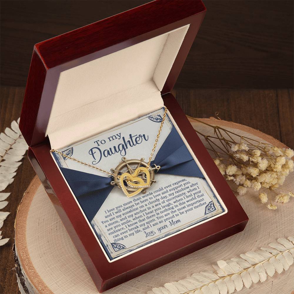 The Daughter-Sunshine Anchor features an Interlocking Hearts necklace with cubic zirconia crystals in surgical steel and rose gold. The decorative box lid, with a blue bow, displays the heartfelt "To my Daughter" note, surrounded by dried flowers on wood.