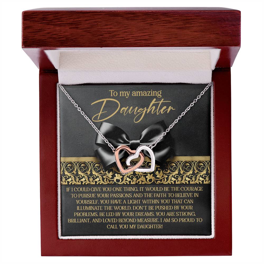 A stunning Interlocking Hearts necklace, finished in rose gold and adorned with cubic zirconia crystals, is elegantly presented in a red box with a black ribbon. The card says "To my amazing Daughter" and features an inspiring message of courage, self-belief, and pride.