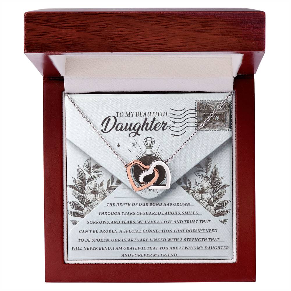 A rose gold Daughter-My Friend Interlocking Hearts necklace rests in an open wooden box. Behind it, a charmingly floral-decorated card titled "To My Beautiful Daughter" enhances the sentiment of this meaningful gift.