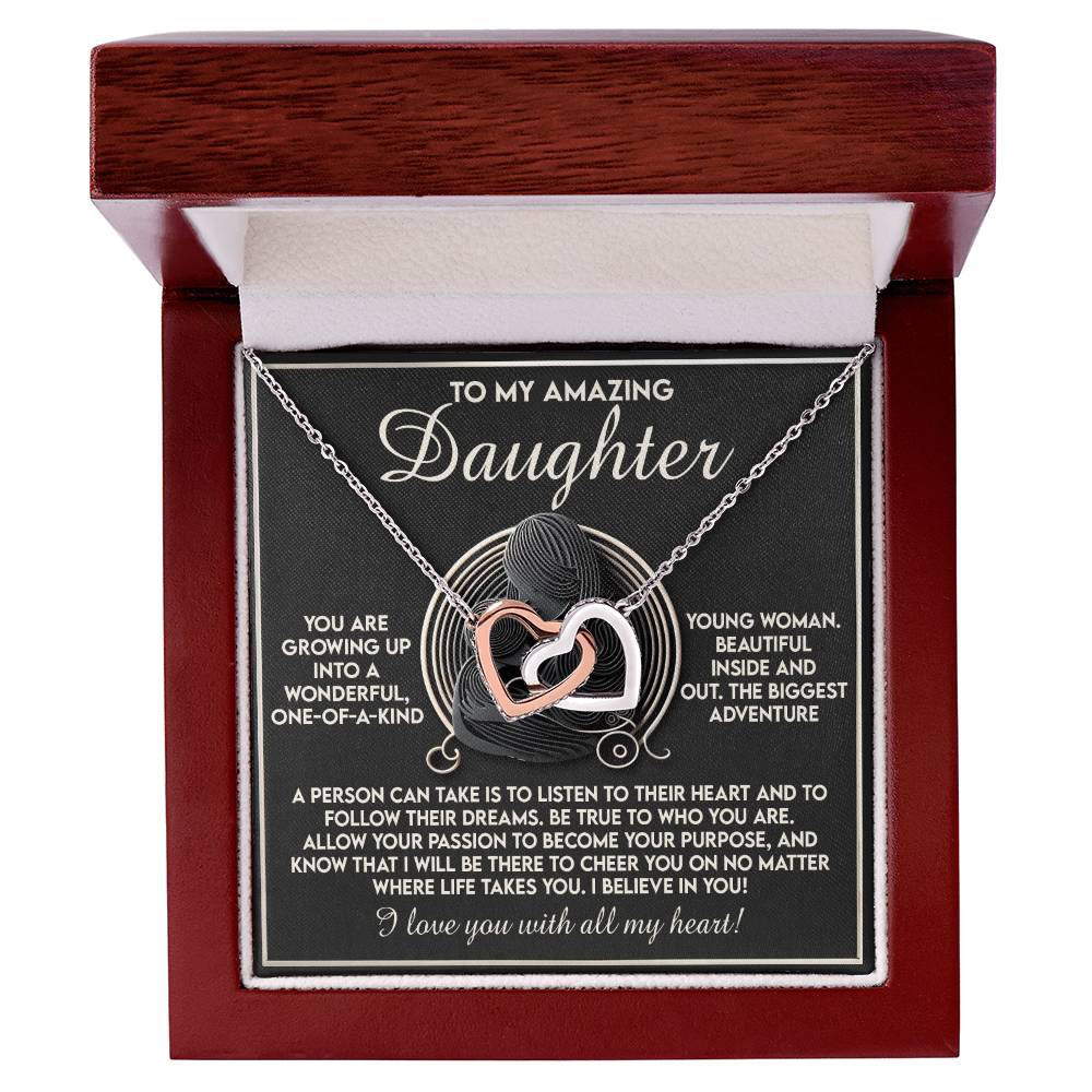 The Daughter-Your Dreams Interlocking Hearts Necklace sparkles with cubic zirconia crystals in an open wooden box. Inside, a heartfelt note about love, dreams, and unwavering support accompanies the message "To my amazing daughter.