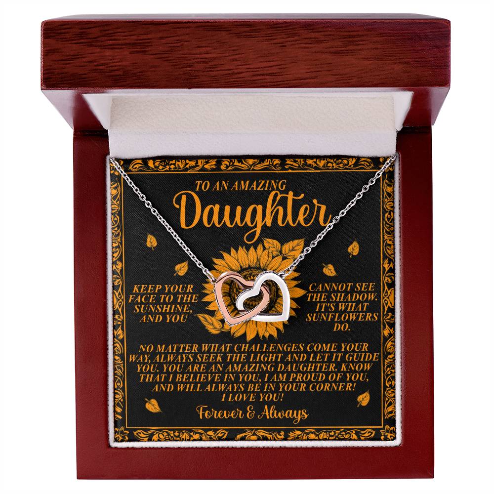 The Daughter-Seek Light - Interlocking Hearts Necklace features a rose gold finish with cubic zirconia crystals, nestled in a red velvet box. It reads: "To an amazing daughter... Keep your face to the sunshine... No matter what challenges come your way... Forever & Always." Sunflower background.