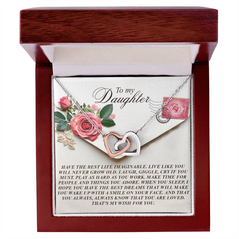 Inside a wooden box, the Daughter-My Wish - Interlocking Hearts Necklace with surgical steel and a rose gold finish awaits. The lid's interior displays a heartfelt message to a daughter with pink roses and an envelope design, highlighting sparkling cubic zirconia crystals.