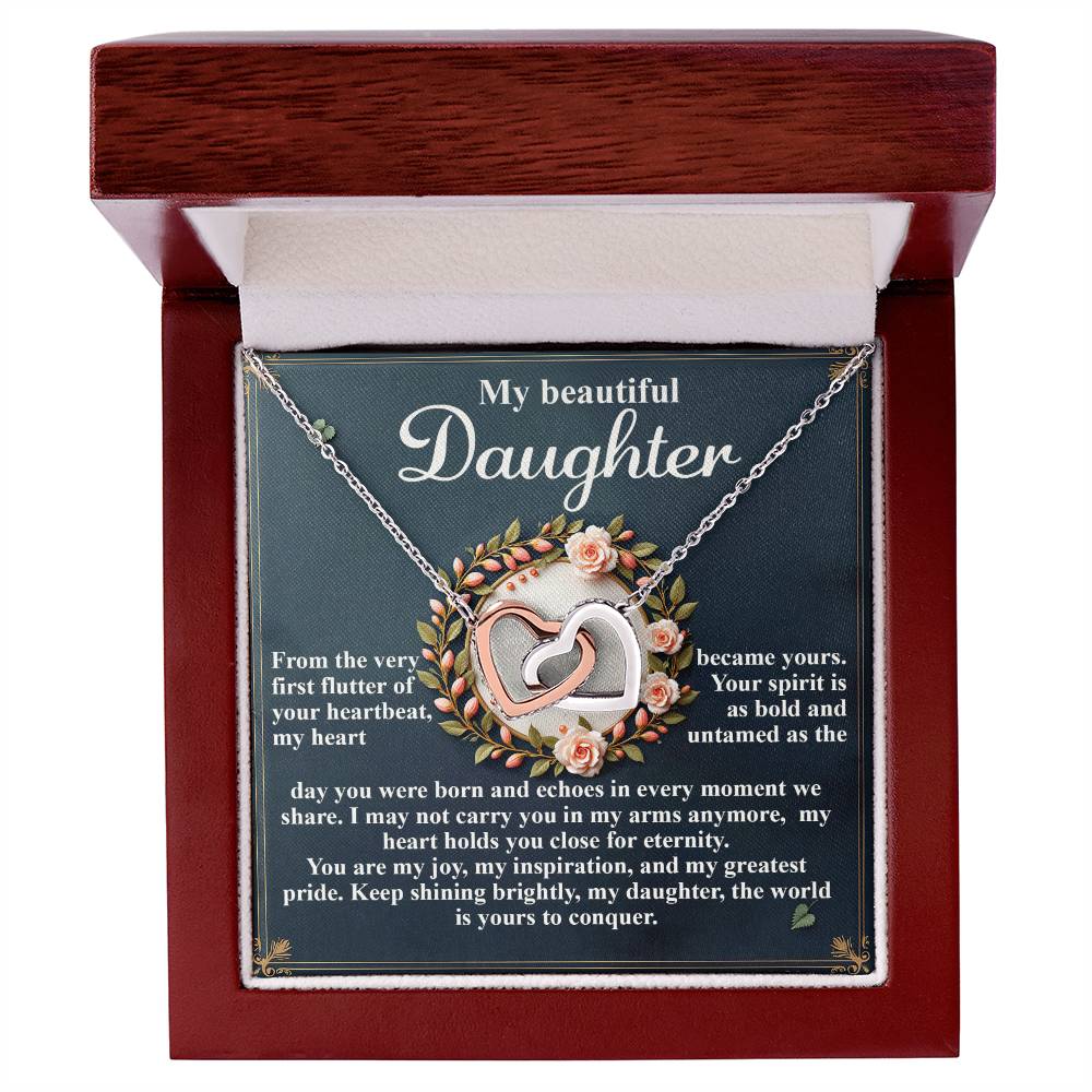 The Daughter-First Flutter Necklace, in a wooden jewelry box, features an interlocking hearts pendant with a shimmering rose gold finish. A heartfelt message from a parent to their daughter highlights her beauty and spirit, expressing love, pride, and encouragement.