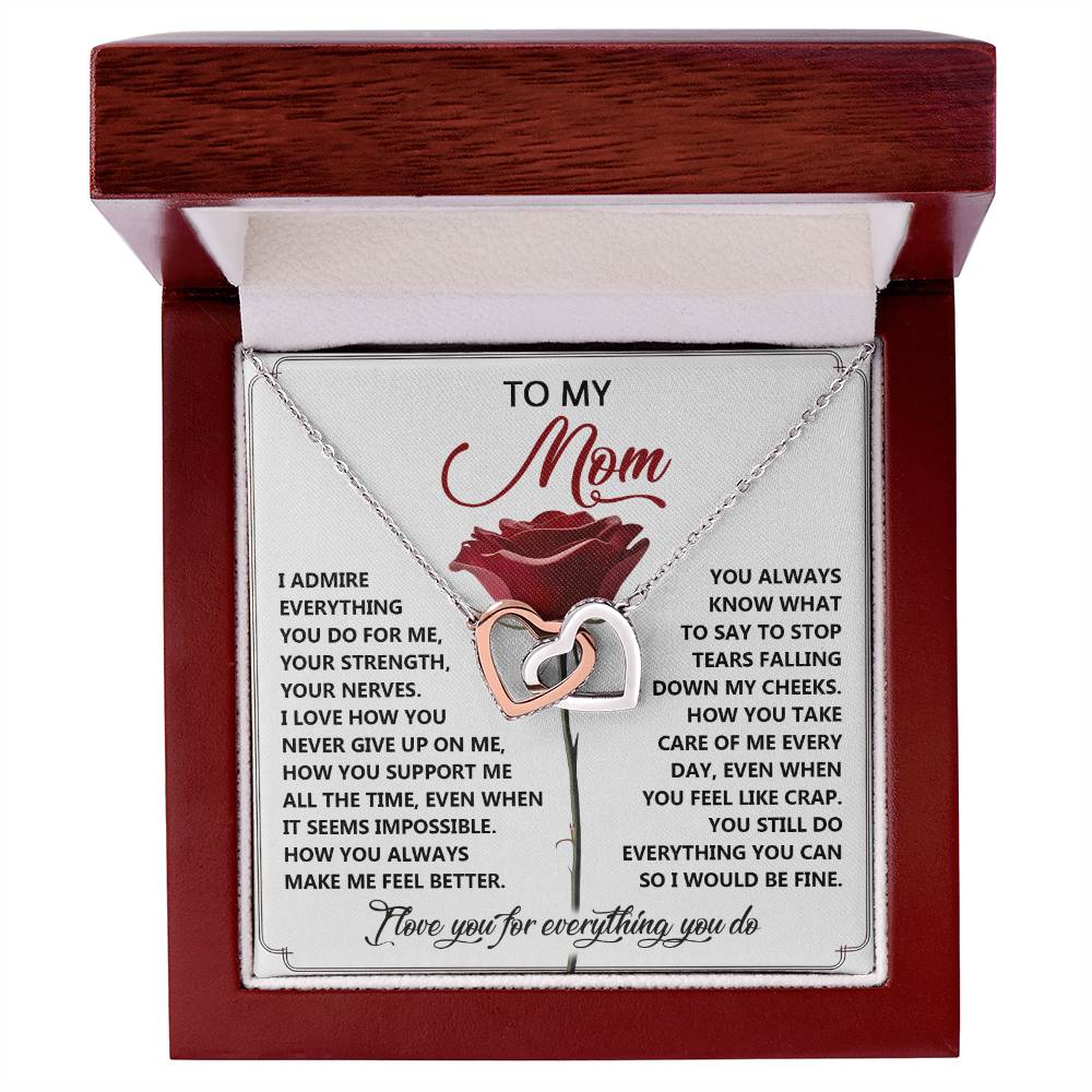 The Mom-Be Fine - Interlocking Hearts Necklace features a surgical steel design with cubic zirconia crystals, stored in a wooden jewelry box. Inside the lid is a heartfelt message to "Mom" with a rose illustration, expressing gratitude for her unwavering love and support.