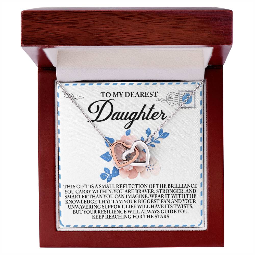 The "Daughter-Brilliance Within" Interlocking Hearts Necklace, finished in rose gold and adorned with cubic zirconia crystals, rests in an open wooden gift box. A heartfelt message inside celebrates a daughter's strength and resilience, making it a meaningful keepsake.