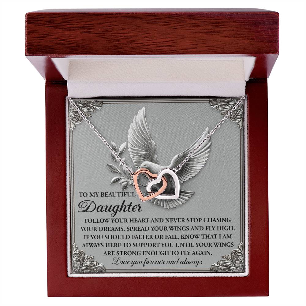The Daughter-Your Wings Interlocking Hearts Necklace is presented in a jewelry box featuring a bird in flight illustration. The necklace, adorned with shimmering cubic zirconia crystals, includes a heartfelt inscription offering love and encouragement to a daughter.