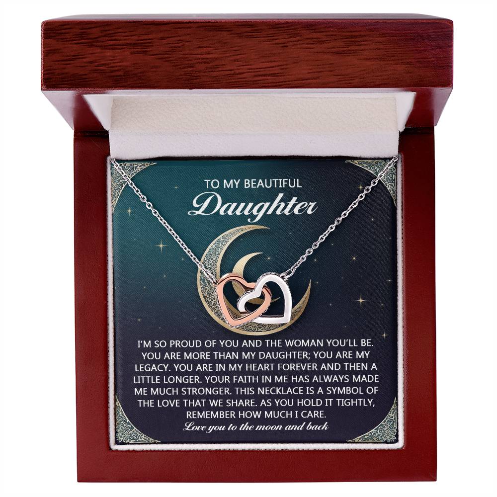 The "Daughter-Hold It Tightly - Interlocking Hearts Necklace" is displayed in a wooden box featuring intertwined hearts and a crescent moon adorned with cubic zirconia. Behind it, the message reads, "To my beautiful daughter," along with a sentimental note about love and legacy.