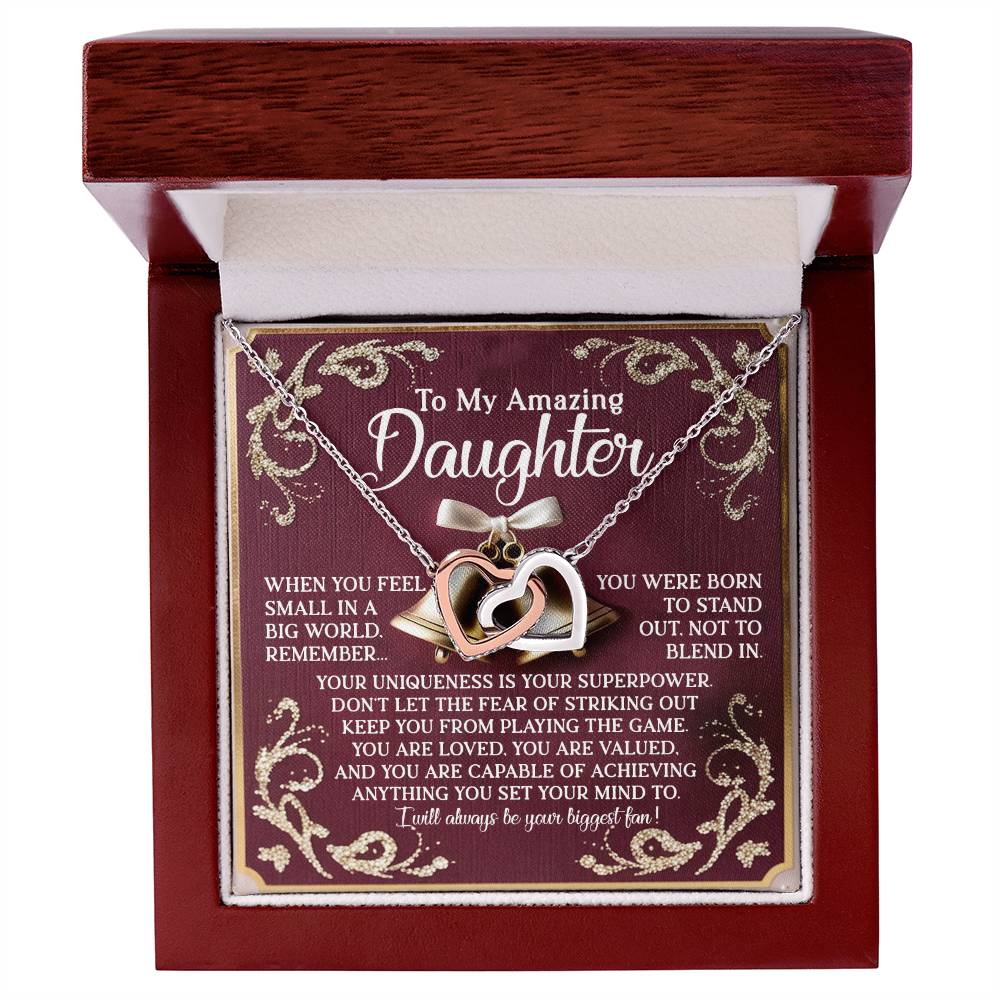 A Daughter-Stand Out Interlocking Hearts Necklace in silver, featuring gold and cubic zirconia hearts, lies in an open wooden box. The interior lid displays an inspirational message for a daughter, surrounded by decorative rose gold accents.