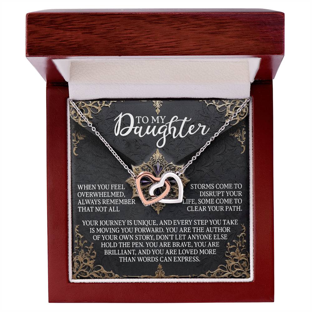The Daughter-The Pen - Interlocking Hearts Necklace features a heart-shaped design with a rose gold finish and cubic zirconia crystals, presented in a wooden box. The message reads: "To my daughter. When you feel overwhelmed, always remember that storms come to disrupt your journey, some come to clear your path….